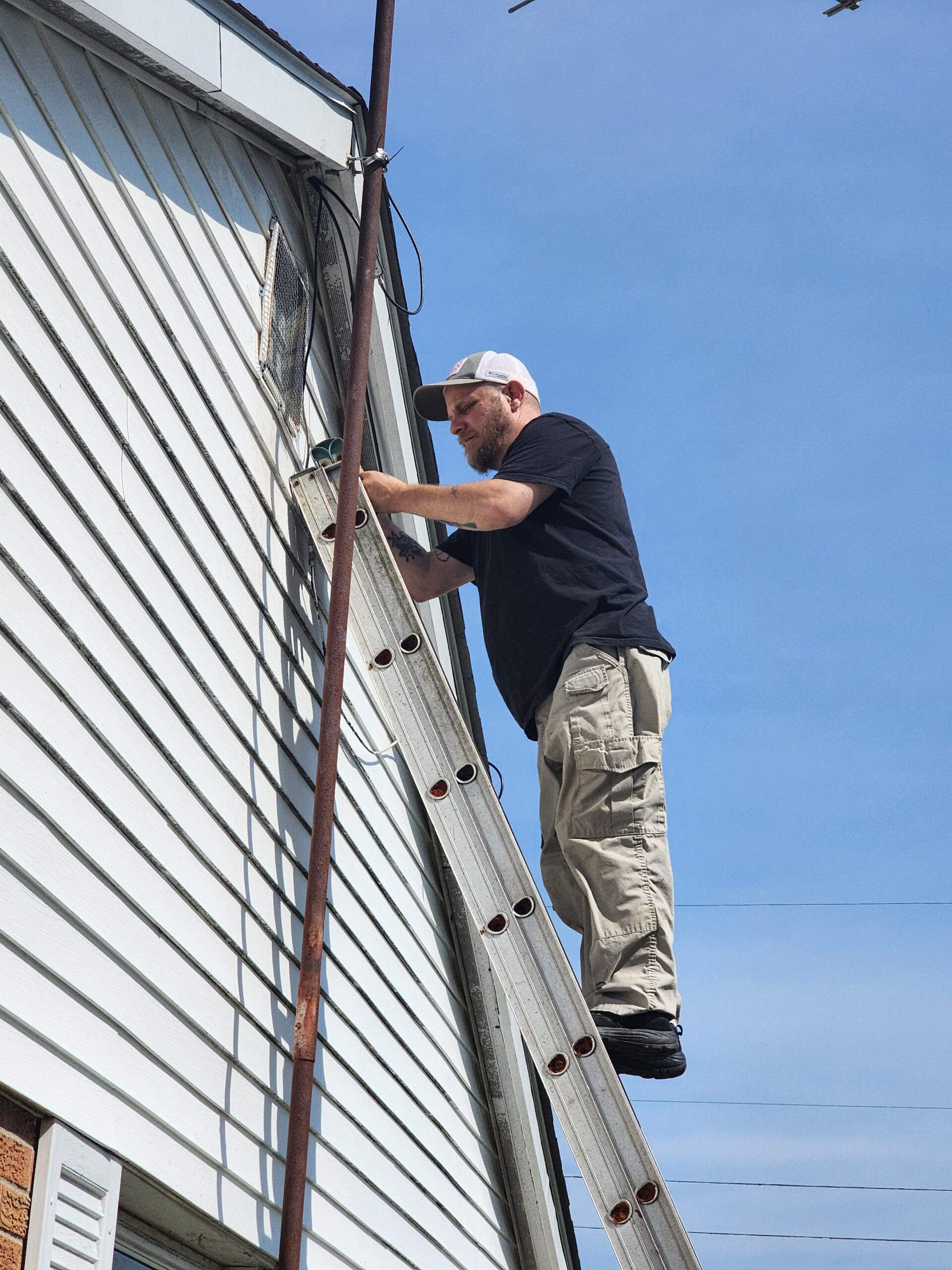 Critter Outlaws technician on a ladder inspecting siding and roofline for entry points